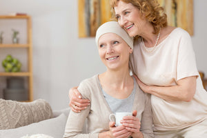Two ladies hugging looking in the distance, with one of them being a cancer survivor drinking tea